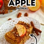 A slice of Baked Apple Oatmeal topped with apple slices and pecans sits on a white plate, with cinnamon sticks and pecans beside it. Other baked oatmeal bars and apples are arranged in the background, creating a cozy, inviting scene.