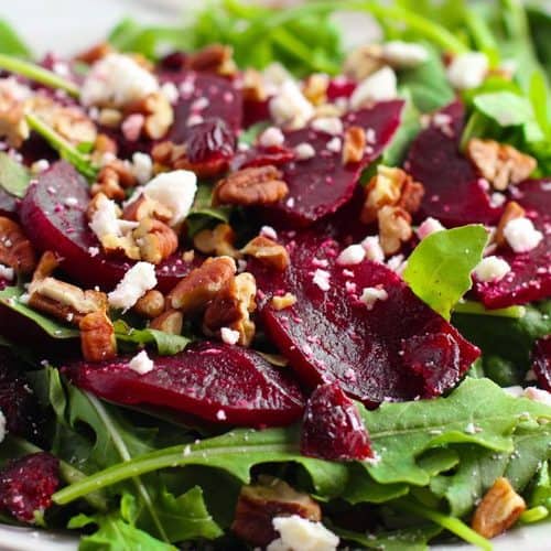 A beet salad with feta, featuring arugula, sliced beets, crumbled cheese, and pecans in a white bowl.