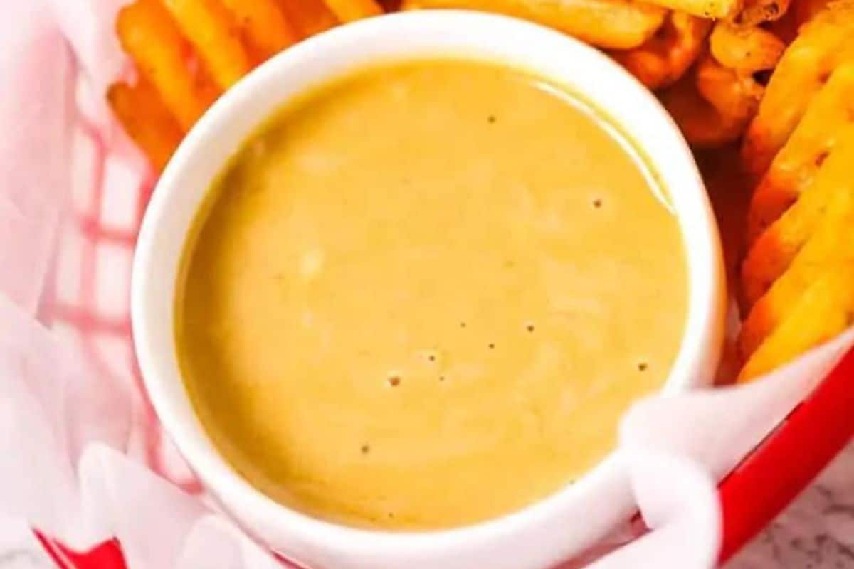 A white bowl filled with creamy sauce, reminiscent of Chick-fil-A's secret recipes, is placed in a red basket alongside crinkle-cut fries.