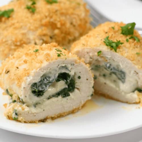 A plate with sliced Chicken Rollatini, featuring creamy spinach filling and a crispy breadcrumb coating, garnished with chopped herbs.