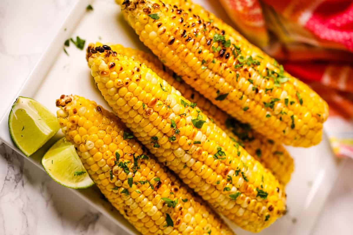 Grilled corn on the cob garnished with chopped cilantro, served on a white plate with lime wedges.