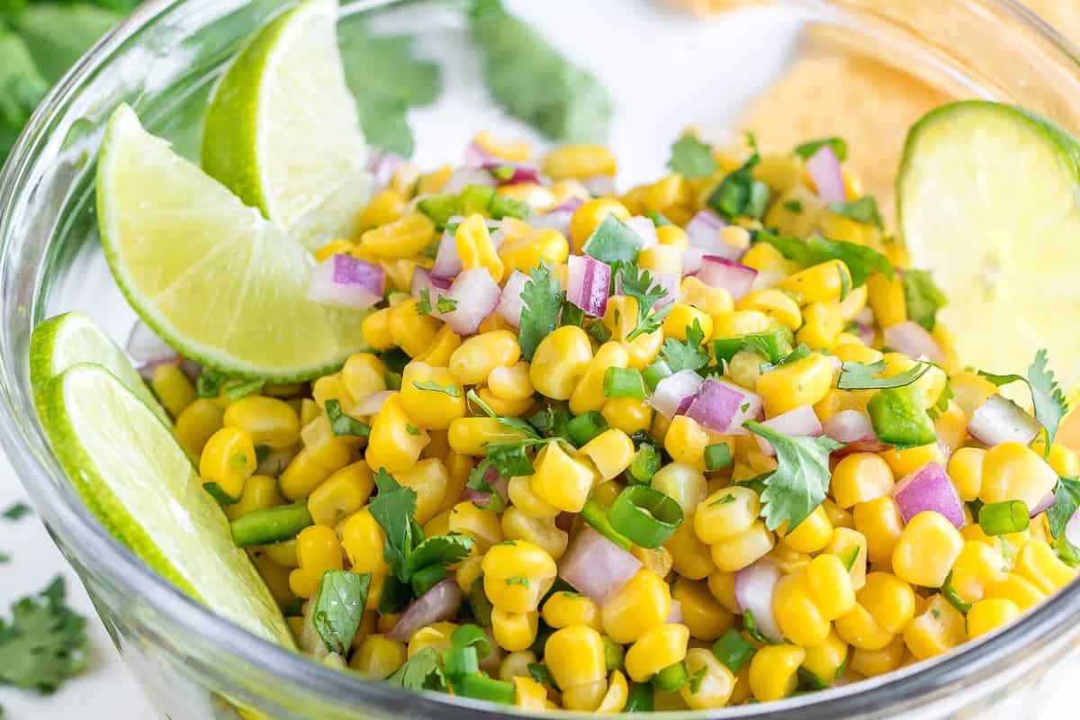 A bowl of corn salad with diced red onions, jalapeños, chopped cilantro, and lime wedges on the side—perfect for recreating Copycat Chipotle Recipes at home.