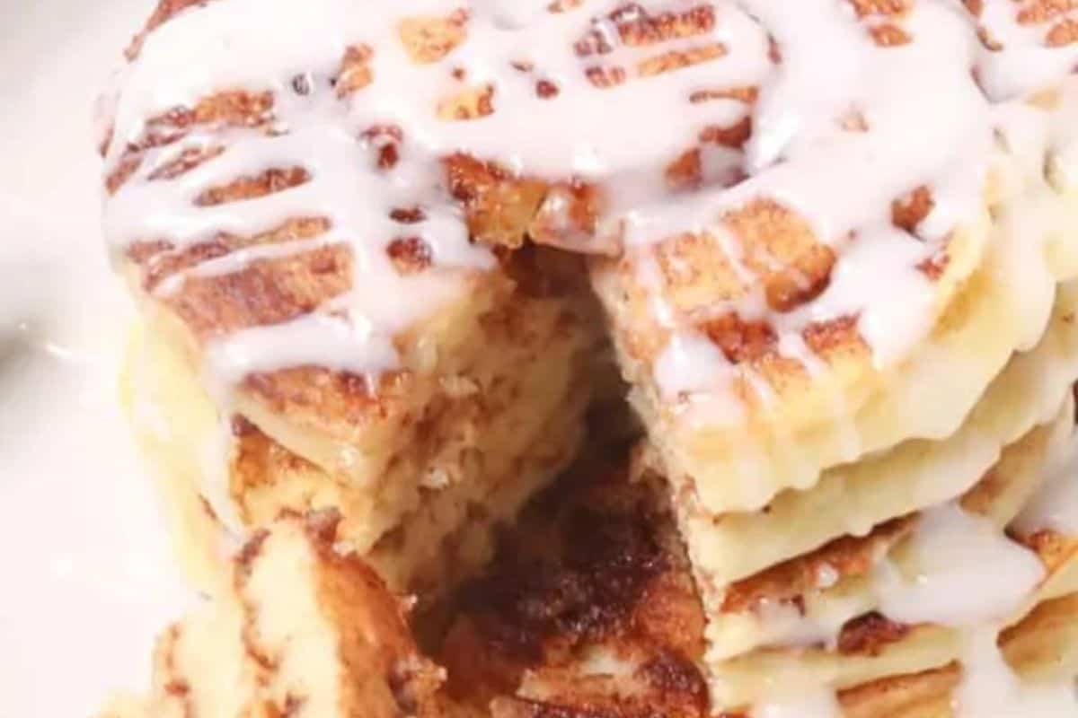 A stack of pancakes drizzled with icing, perfect for your weekend brunch. A wedge is cut out, tempting you to discover why this creation tops the list of everyone's favorite pancake recipes.