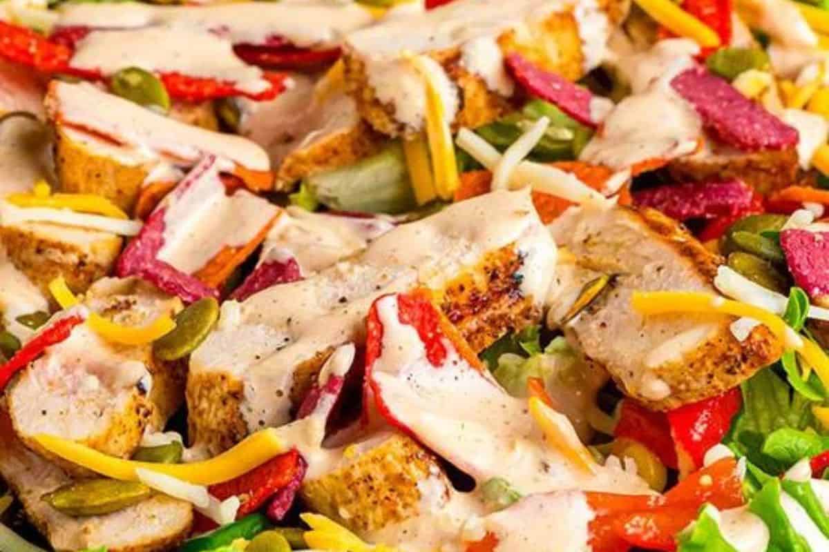 Close-up of a salad with grilled chicken pieces, sliced red peppers, mixed greens, shredded cheese, and a creamy dressing inspired by Chick-fil-A recipes you can make at home.