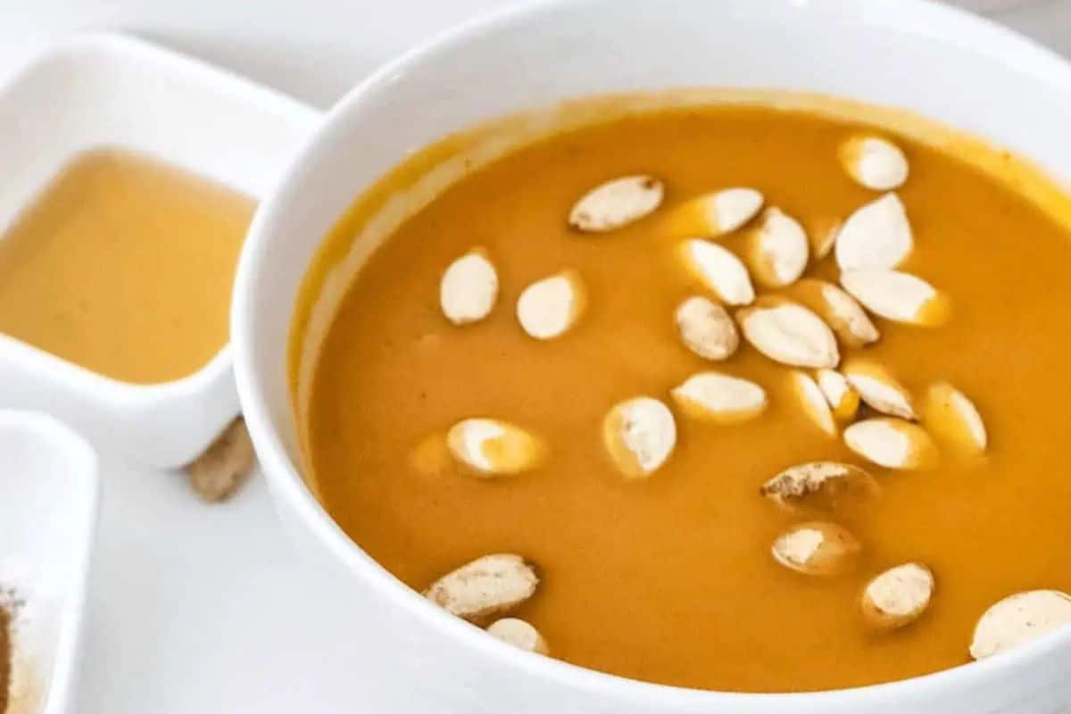 Close-up of some orange squash soup in a white bowl, garnished with some pumpkin seeds.