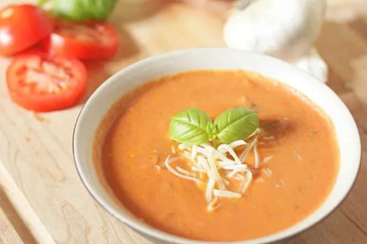 Close-up of a creamy basil tomato soup in a white bowl, garnished with some white cheese and basil.