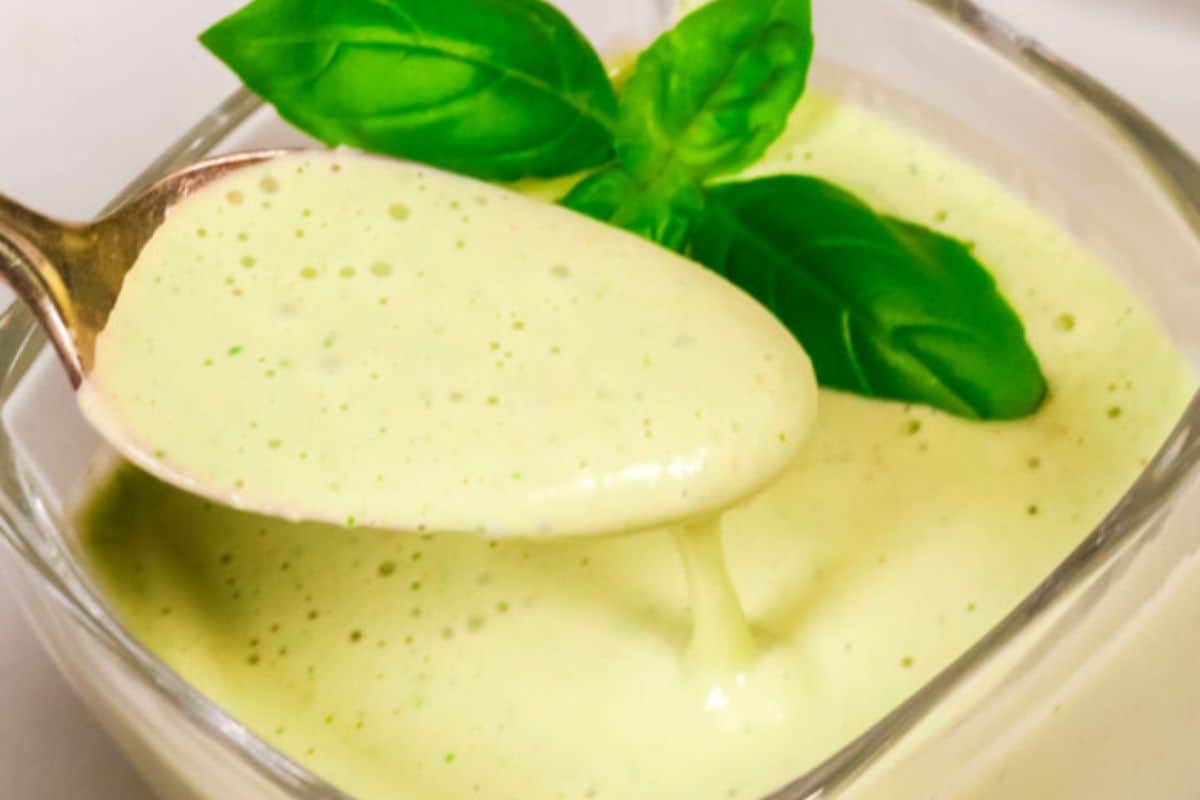 Close-up of some green goddess dressing on a spoon, dripping into a glass.