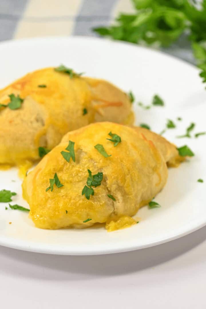 Two golden-brown chicken roll ups rest on a white plate, garnished with chopped green herbs.