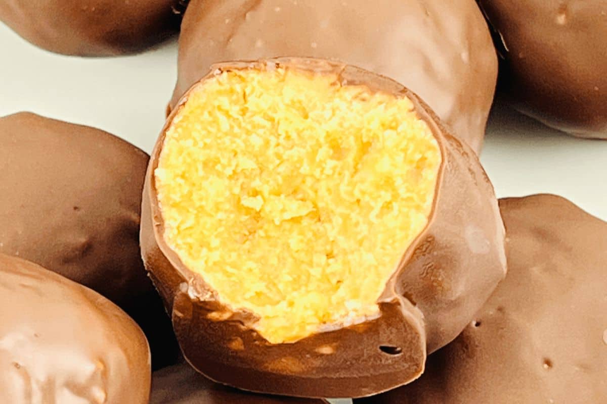 A close-up image of a bite-sized chocolate-covered orange confection with the interior showing a bright orange filling, truly one of those must-try recipes.