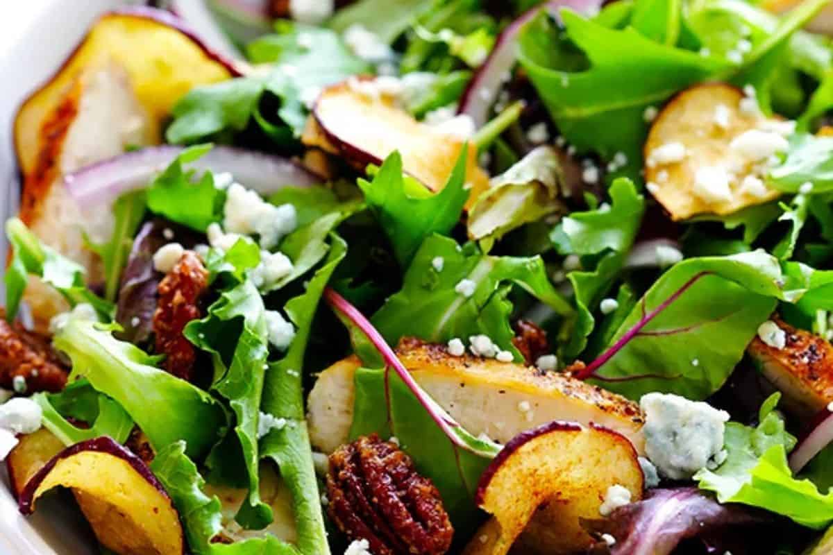 A close-up of some Fuji apple chicken salad, served with arugala, red onions, chicken, pecans, and blue cheese crumbles.