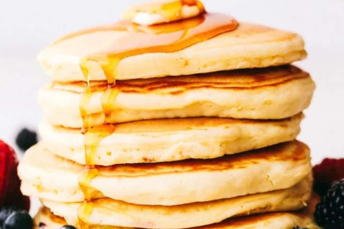 A stack of pancakes topped with butter and drizzled with syrup, surrounded by assorted berries—a perfect weekend treat for those who love trying new pancake recipes.