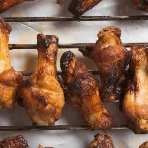 Several cooked chicken wings are arranged on a metal rack over white parchment paper, making them a perfect addition to your autumn tailgating recipes.