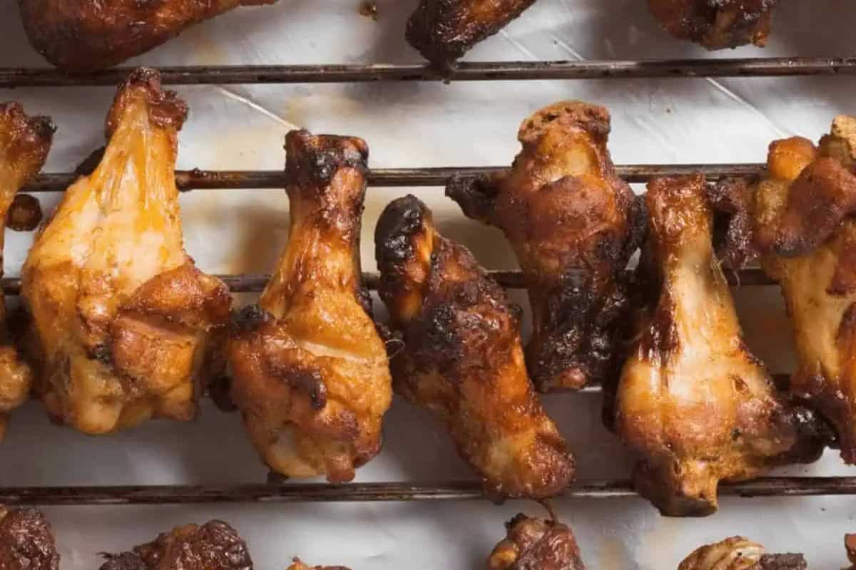 Several cooked chicken wings are arranged on a metal rack over white parchment paper.
