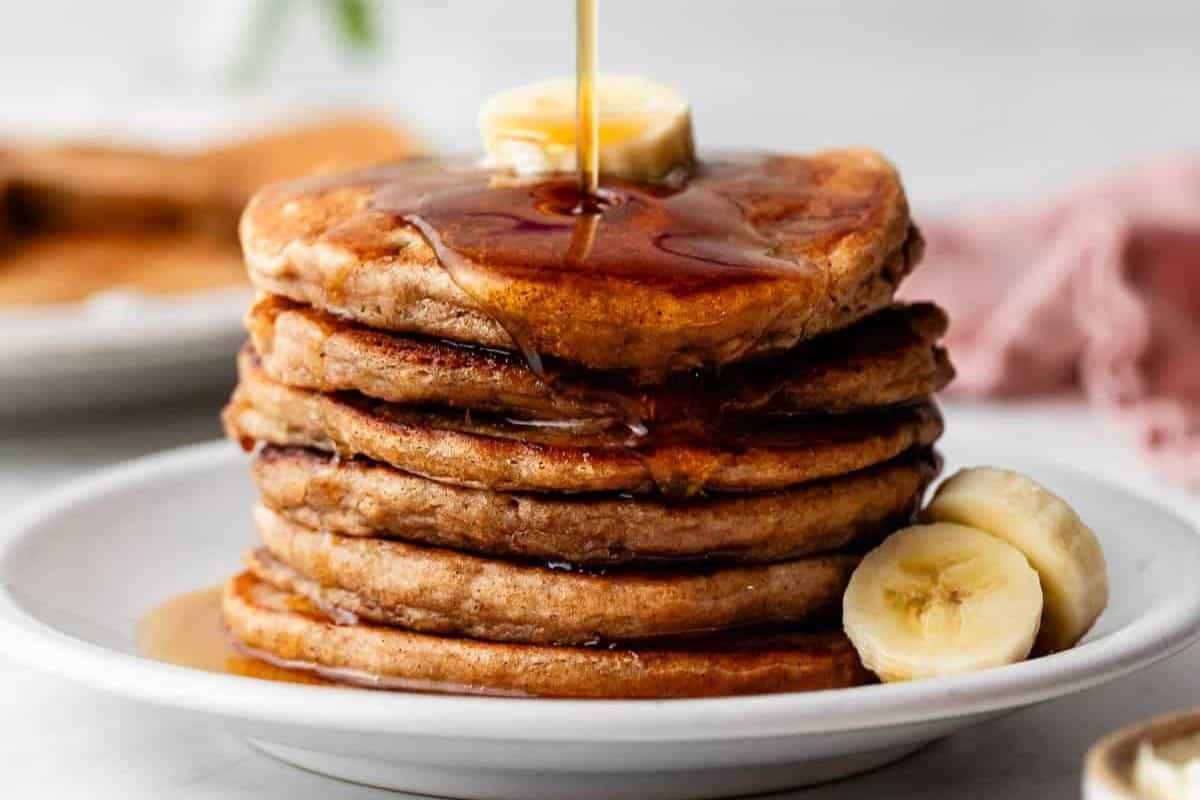 A stack of pancakes topped with sliced banana and syrup on a white plate offers a delightful weekend breakfast idea.