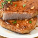 A fork pierces a juicy, cooked pork chop with garlic and herbs on a white plate, perfectly capturing the essence of delicious Honey Garlic Pork Chops.