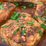 Close-up of seasoned and cooked chicken breasts garnished with chopped parsley, served in a sauce in a pan reminiscent of the flavors found in Honey Garlic Pork Chops.