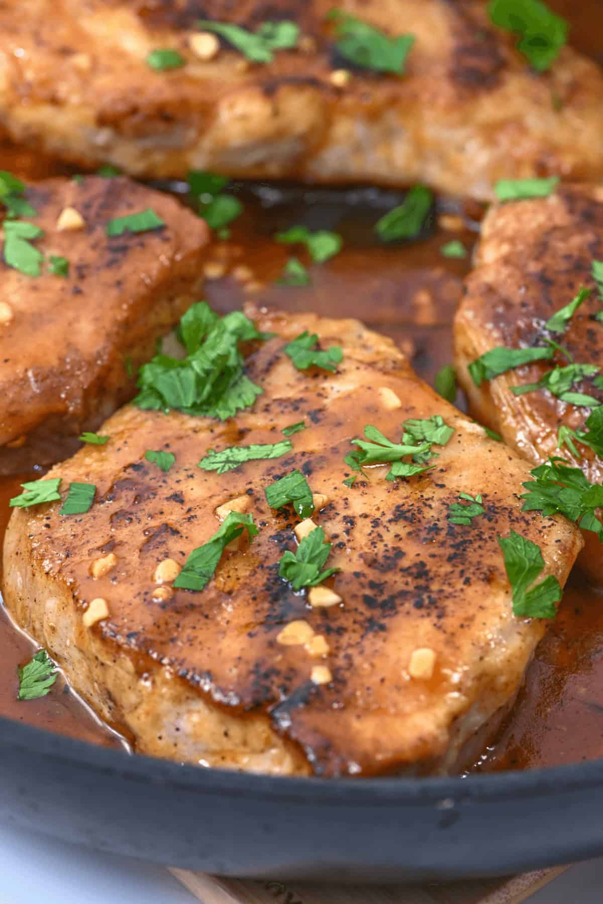 Close-up of seasoned and cooked chicken breasts garnished with chopped parsley, served in a sauce in a pan reminiscent of the flavors found in Honey Garlic Pork Chops.
