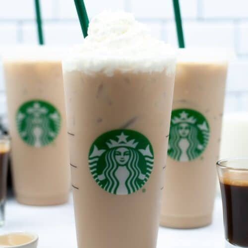 Three Iced White Chocolate Mochas topped with whipped cream and green straws, with a small shot of espresso in the foreground.