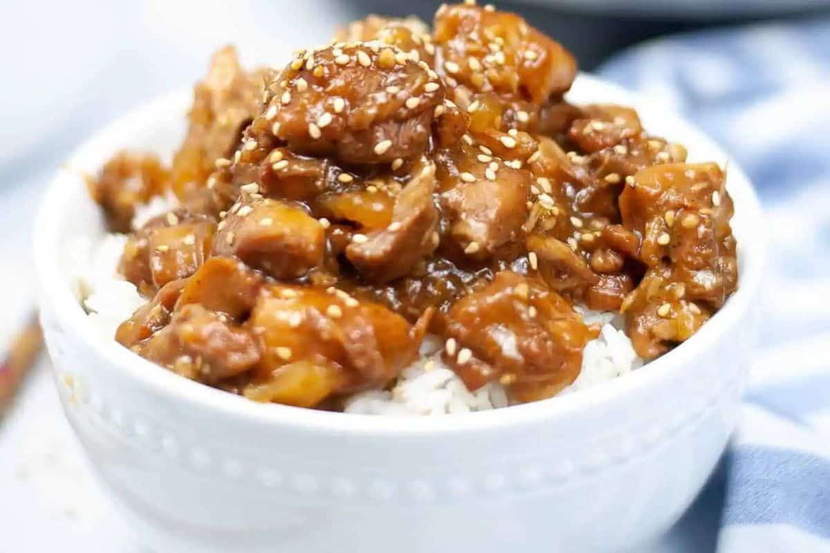 A white bowl filled with white rice topped with pieces of saucy chicken and sprinkled with sesame seeds—this is a must try for anyone who loves Asian dishes.