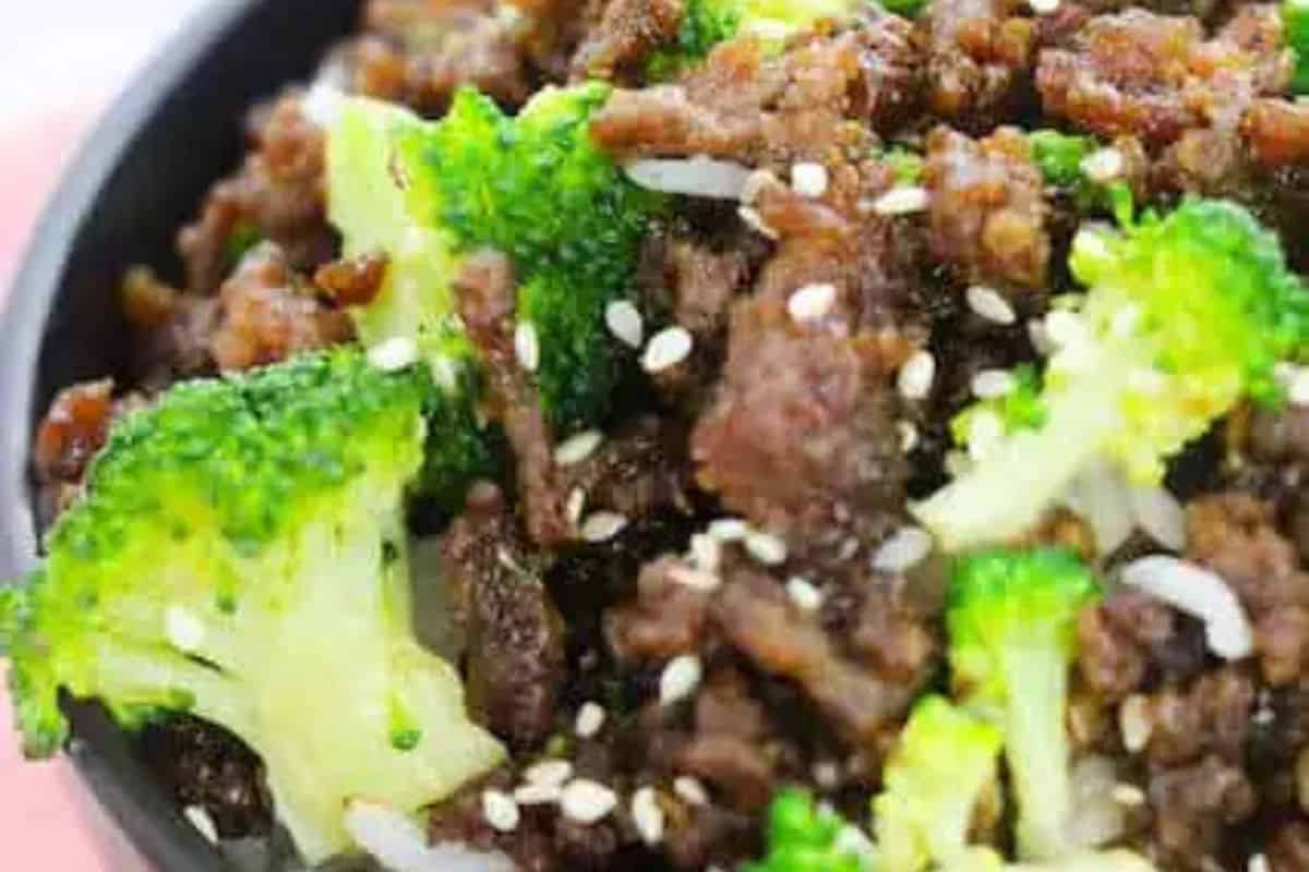 A close-up of a bowl containing cooked ground beef, broccoli florets, white rice, and sprinkled sesame seeds—this is a must try for fans of Asian dishes.