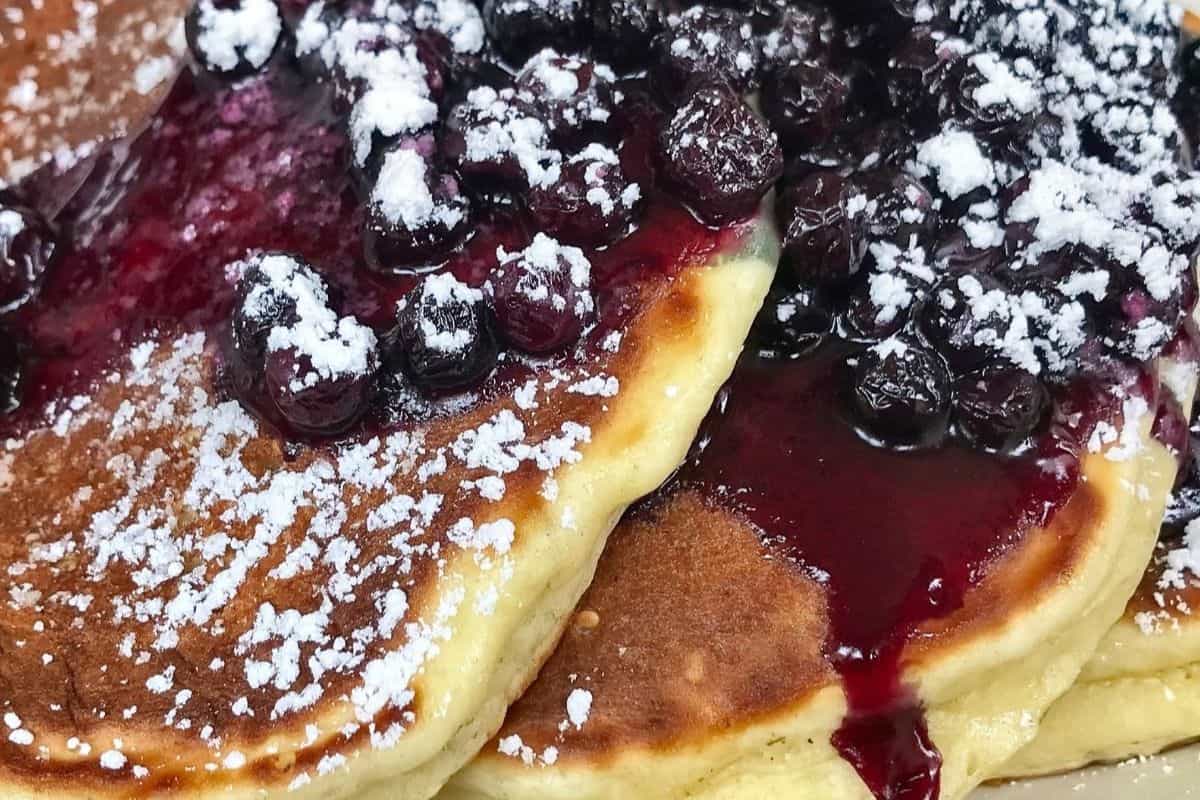 A close-up of pancakes topped with blueberry sauce and powdered sugar, perfect for indulging in your favorite pancake recipes this weekend.