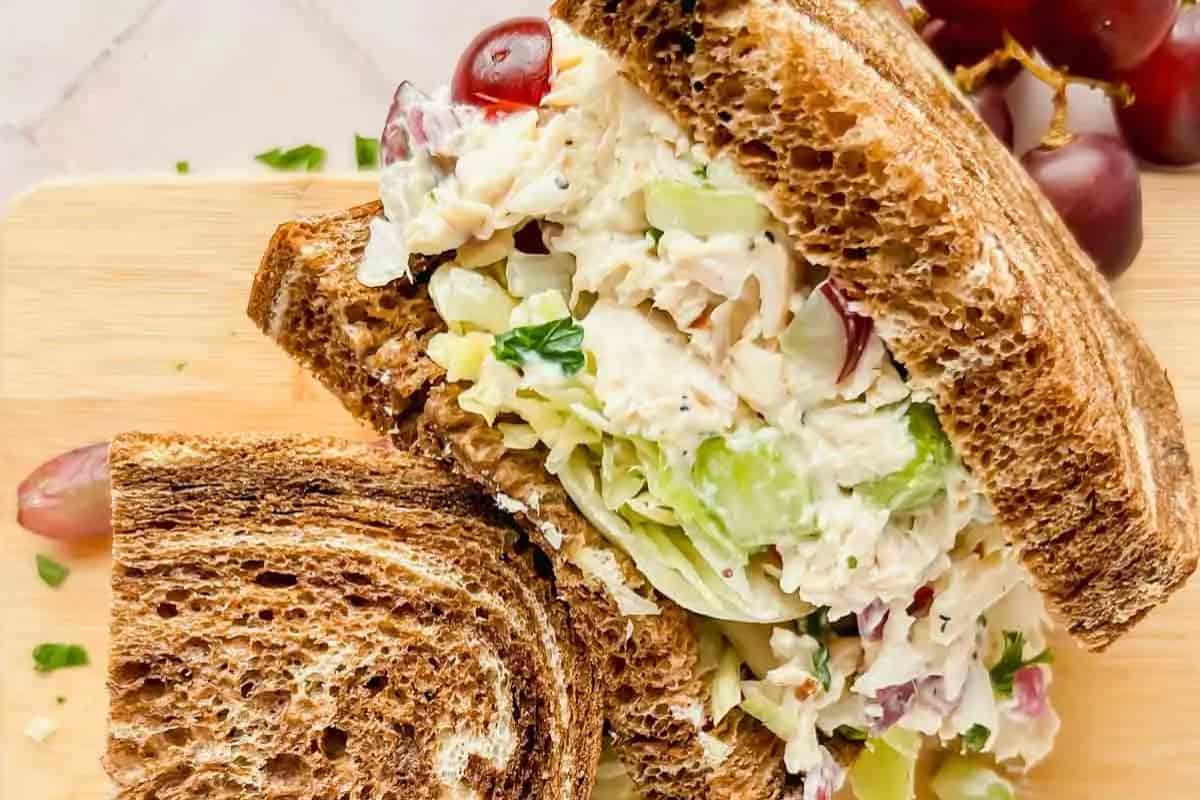 Close-up of a chicken salad sandwich, served on marble bread with grapes on the side.