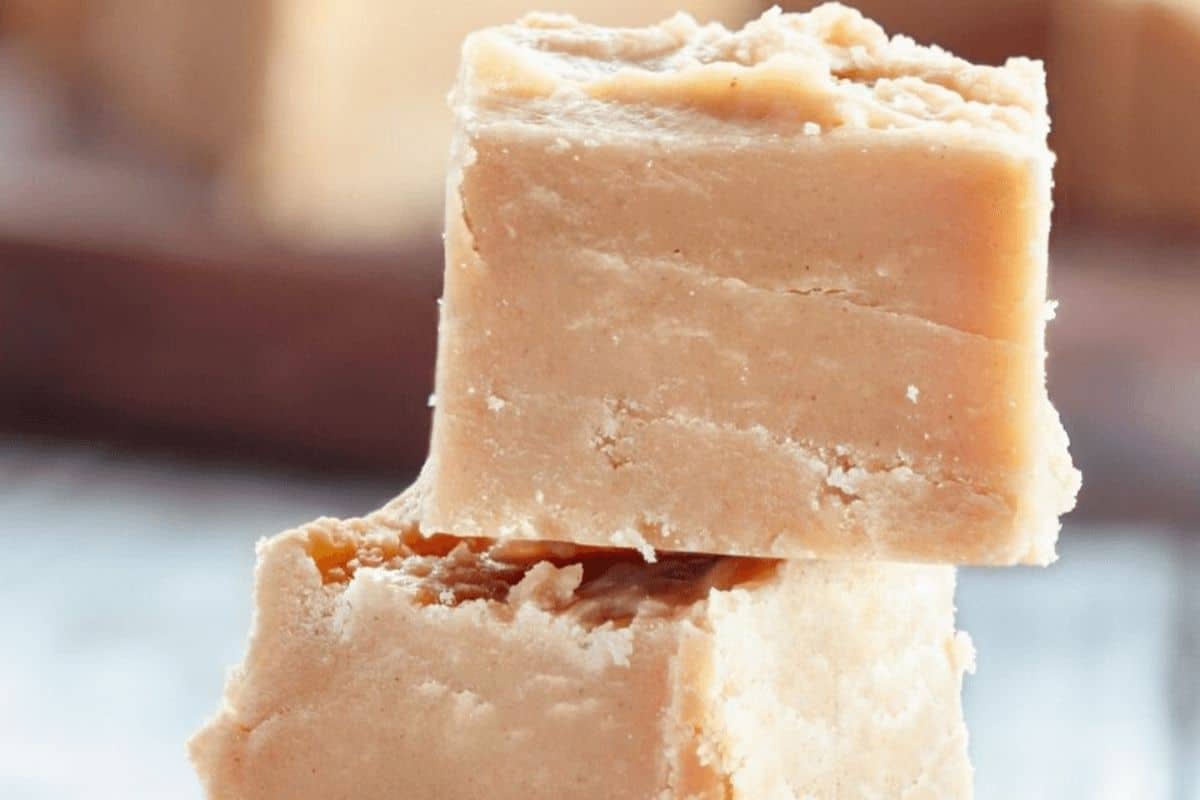 Close-up of two light brown fudge squares stacked on top of each other. The texture appears creamy and slightly crumbly, making them a must-try for those exploring new recipes.