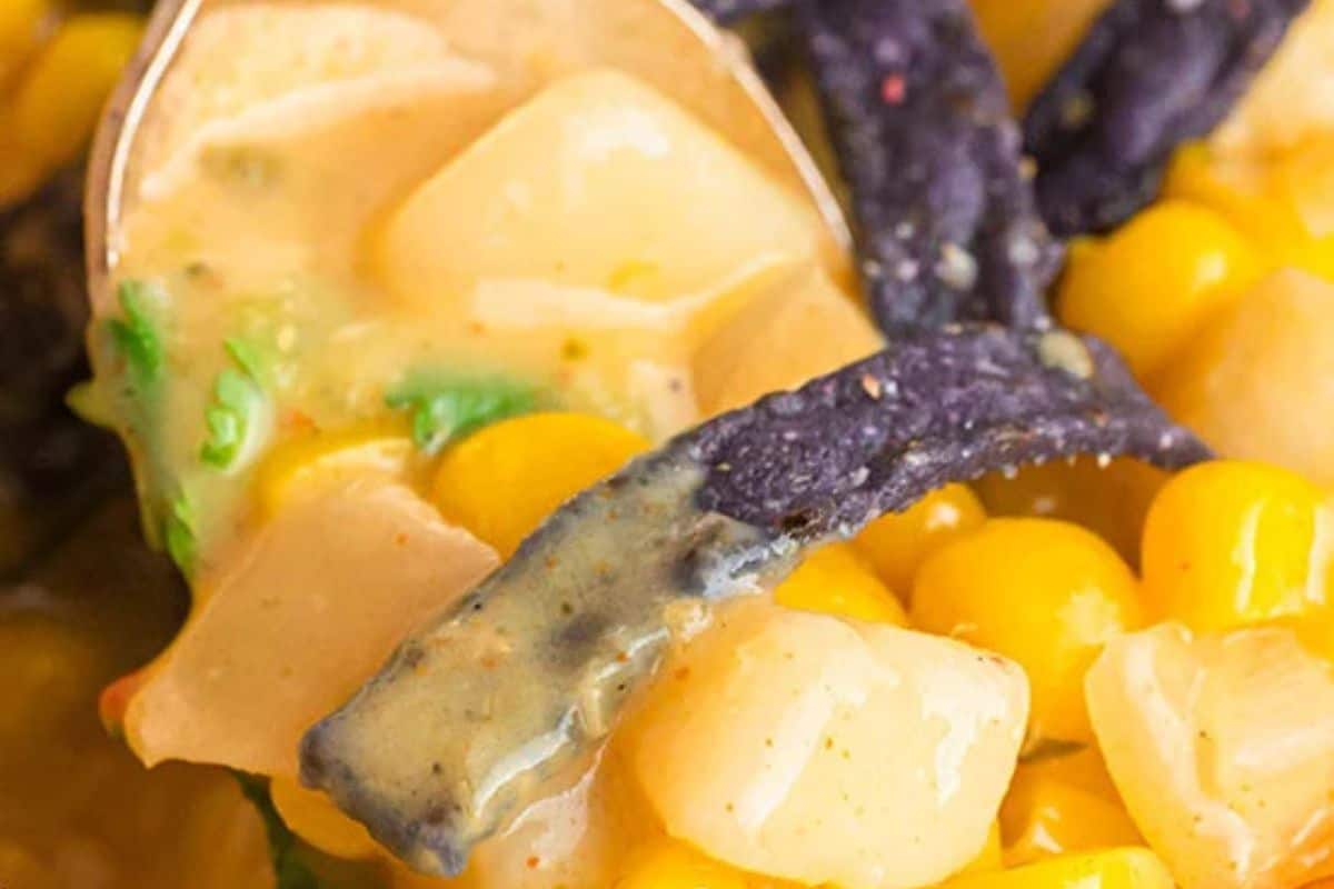 Close-up of some Mexican street corn chowder on a spoon, granished with some blue corn tortilla strips.