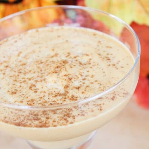 A glass of creamy Pumpkin Spice White Russian dessert topped with cinnamon, with autumn leaves blurred in the background.