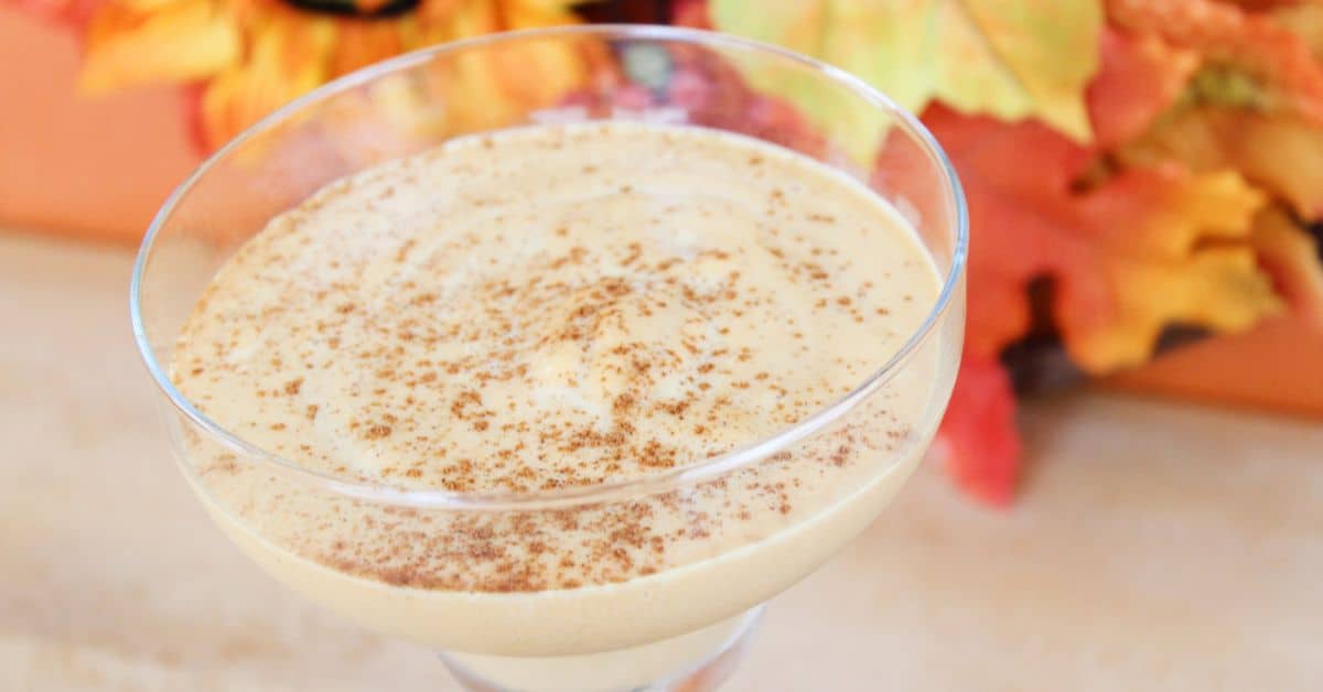 A glass of creamy Pumpkin Spice White Russian dessert topped with cinnamon, with autumn leaves blurred in the background.