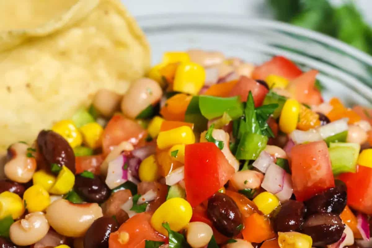 A close-up of a redneck caviar with black and white beans, corn, diced tomatoes, onions, and cilantro, served next to tortilla chips.