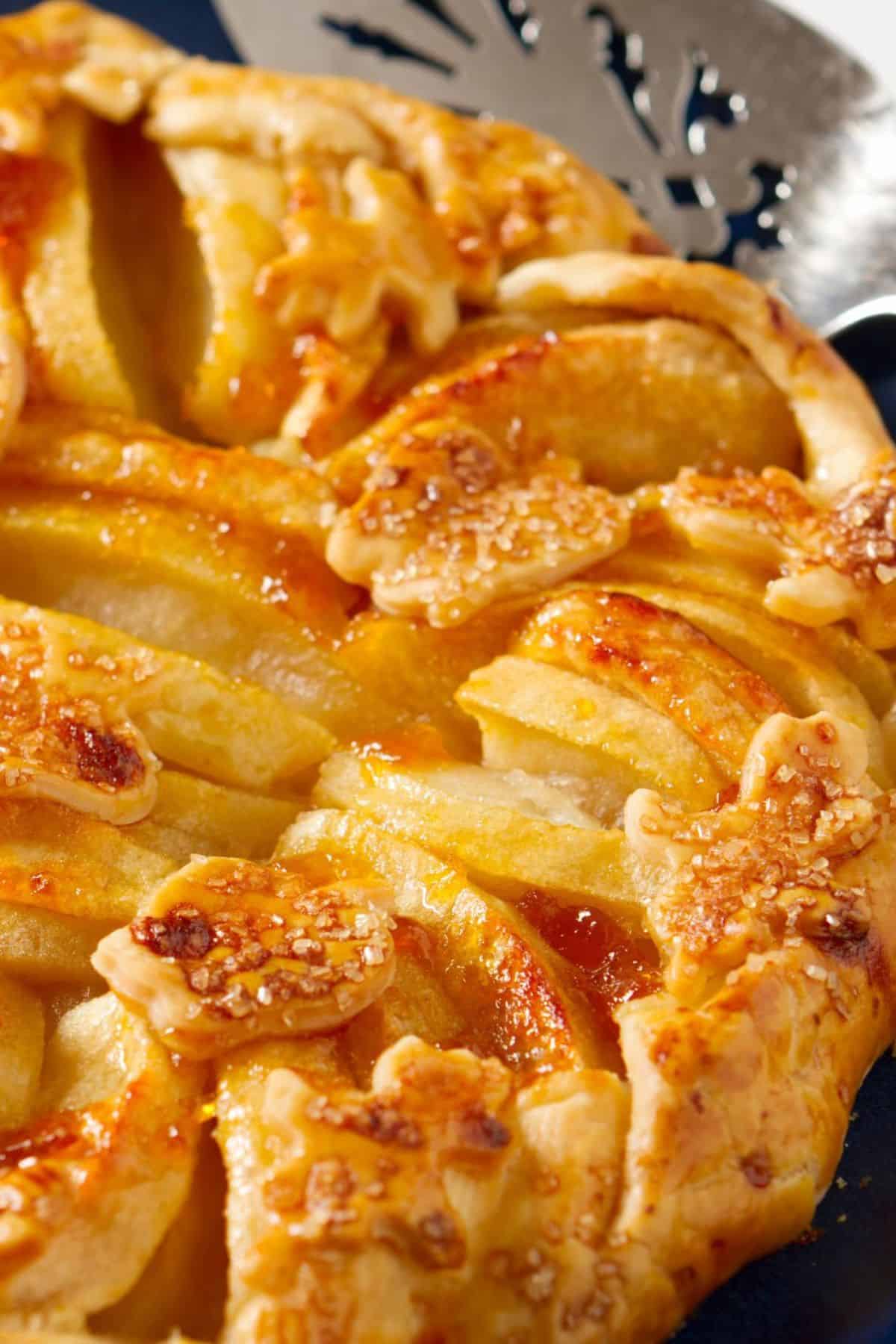 Close-up of a golden-brown dessert detail and sugar crystals on top, next to a metal pie server.