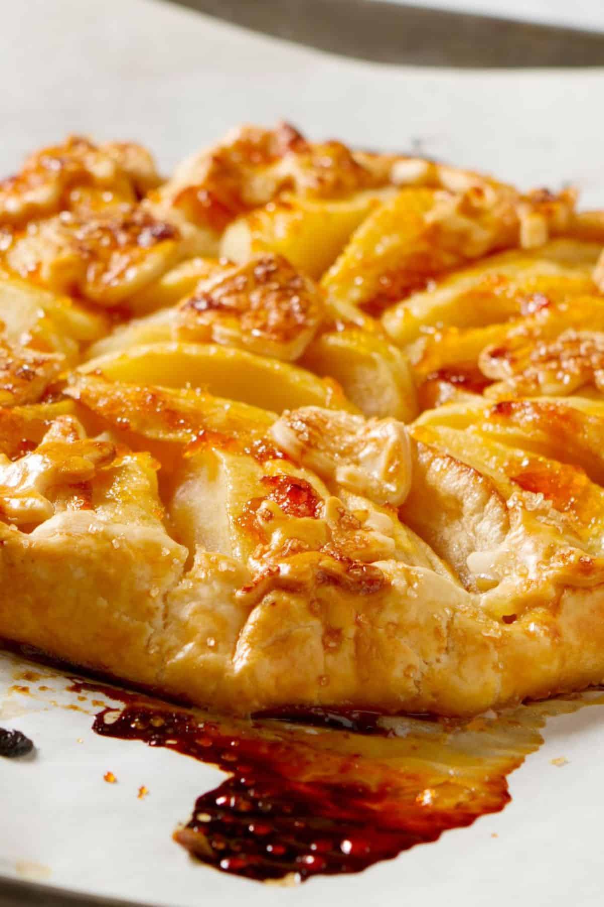 A close-up of a rustic pear galette with golden, flaky crust and caramelized edges, baked on parchment paper, reminiscent of a classic Rustic Apple Tart.