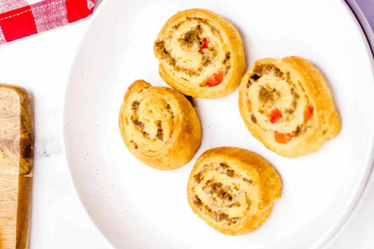 Four sausage pinwheels with visible bits of sausage and red pepper on a white plate.