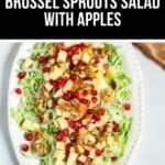A white oval plate with Shaved Brussel Sprouts Salad with Apples, topped with walnuts and pomegranate seeds.