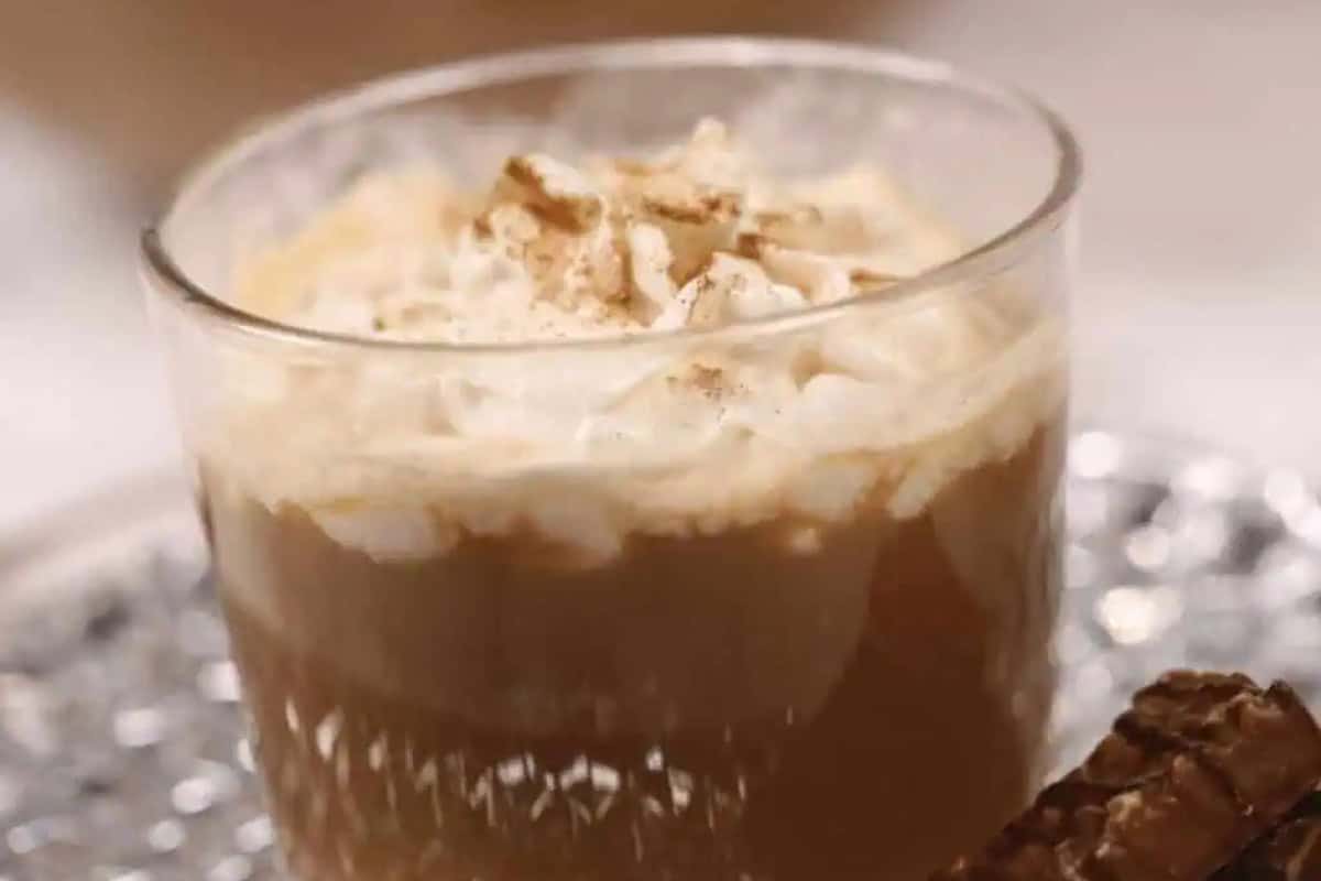 A glass of Southern coffee punch  topped with whipped cream and a sprinkle of cinnamon sits on a silver tray next to a chocolate-covered wafer