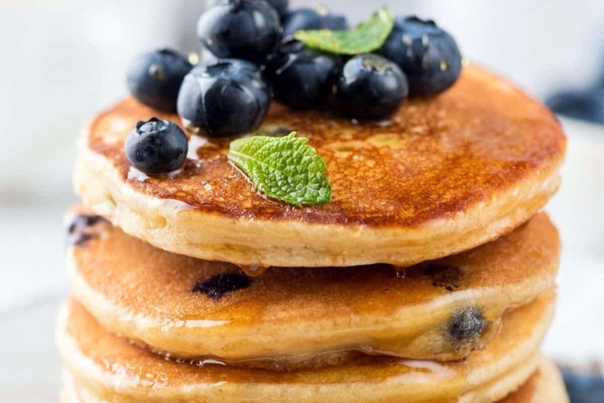 Enjoy a weekend treat with a stack of pancakes topped with blueberries and a mint leaf, drizzled with syrup. Perfect for those exploring new pancake recipes!