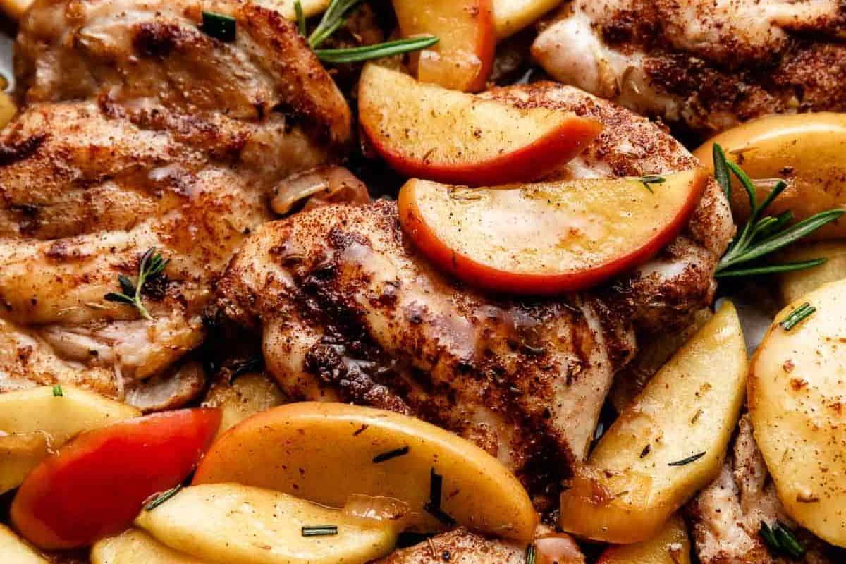 Close-up of cooked, seasoned chicken with sliced apples and sprigs of rosemary—perfect comfort food for those who love comforting fall meals.