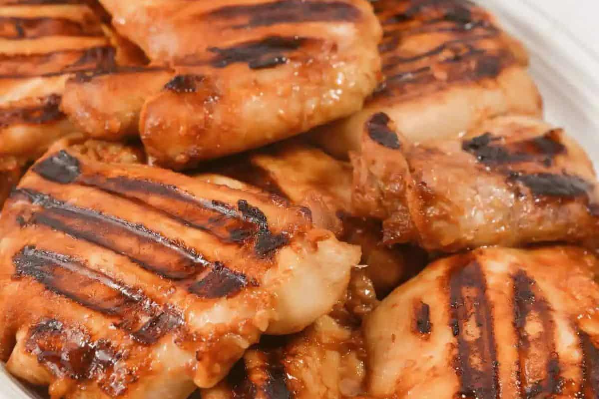 Grilled pieces of chicken with visible char marks are stacked on a white plate—an Asian dish that's a must try and definitely better than takeout.