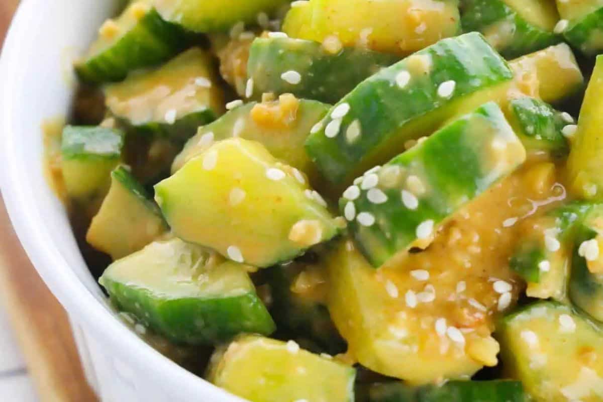 Close-up of chopped cucumber tossed in a creamy dressing and topped with sesame seeds, served in a white bowl—a must try for fans of Asian dishes.