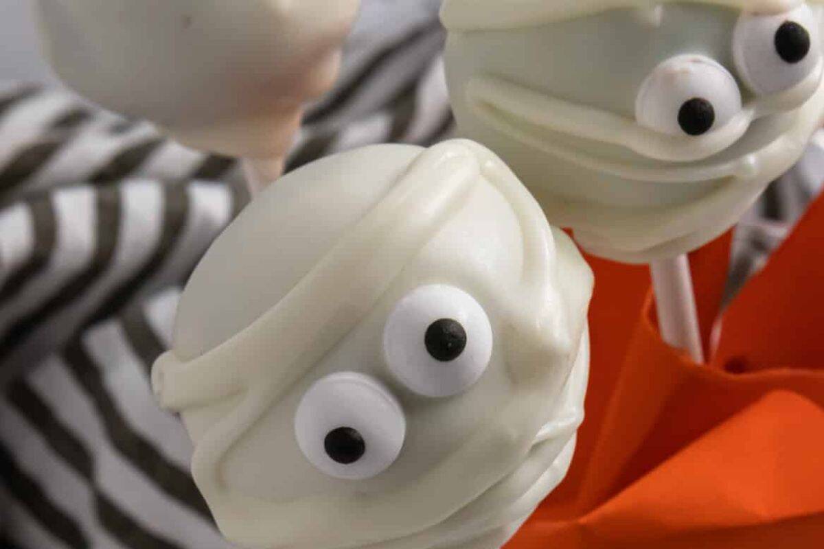 Close-up of cake pops decorated as mummies, wrapped in white icing with small candy eyes peeking through the frosting.