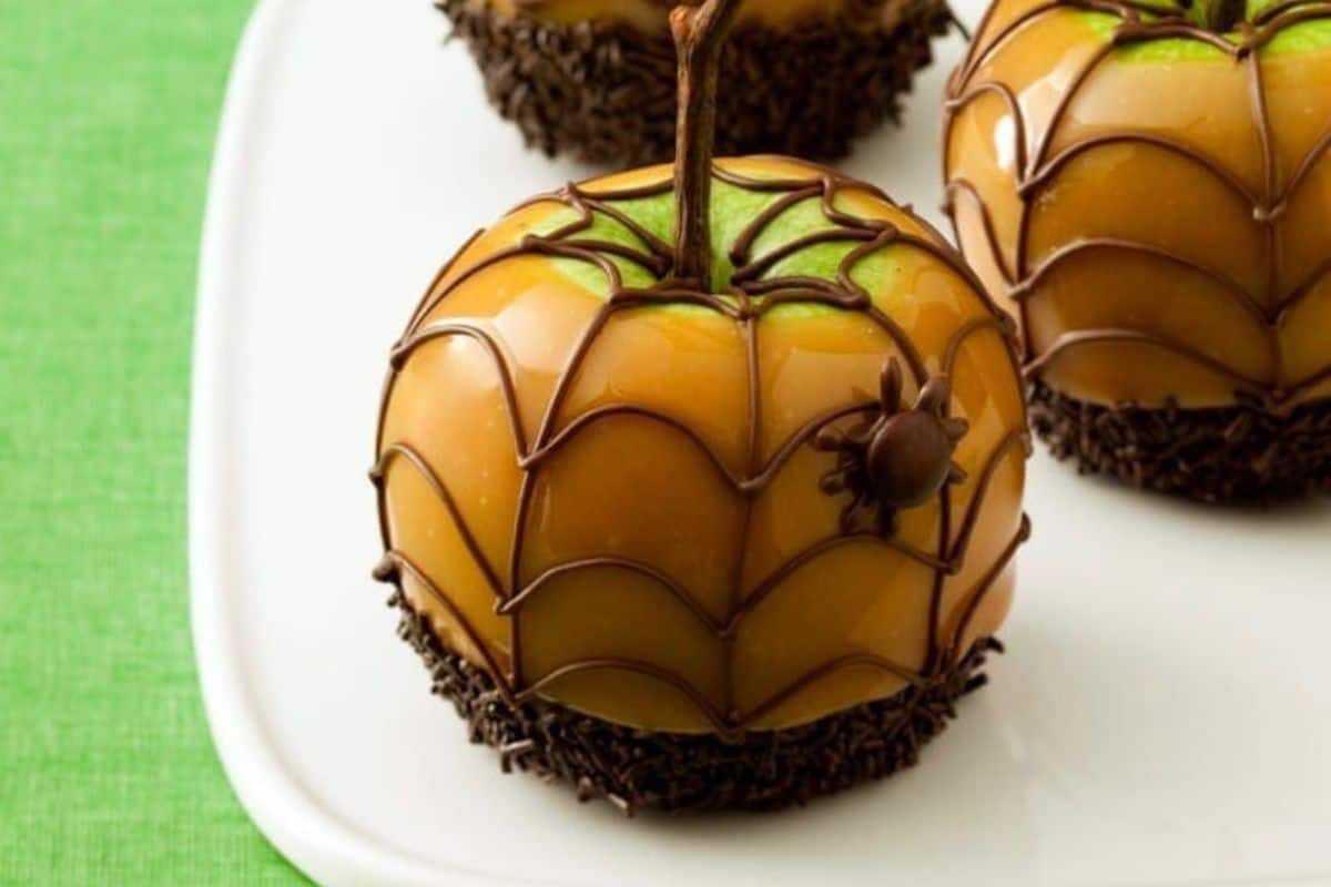 Caramel apples coated with a rich chocolate drizzle, topped with a decorative chocolate spider and sprinkles.