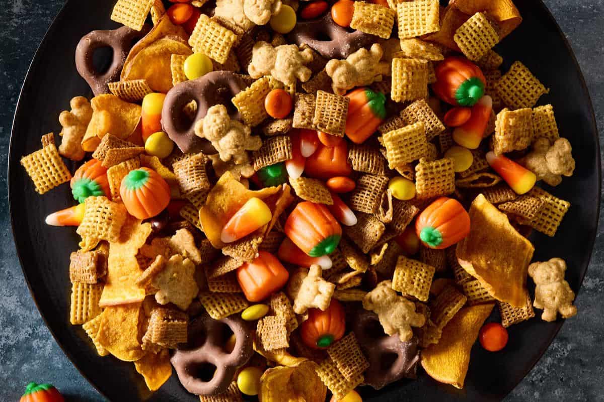 Close-up of Halloween Chex mix featuring a colorful blend of cereal pieces, candy, pretzels, and graham crackers, topped with festive orange pumpkins.