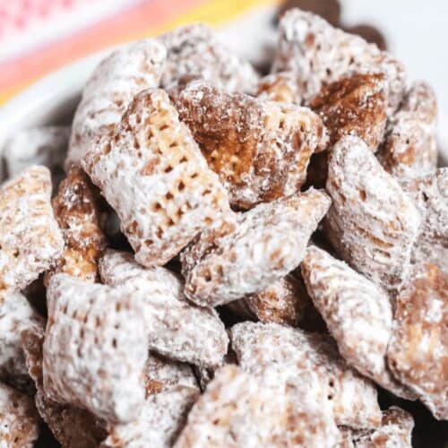A bowl of cereal squares coated in powdered sugar, with chocolate pieces scattered in the background, makes for one of the easiest snack mix recipes. Perfect for those seeking quick snack recipes that satisfy both sweet and crunchy cravings.