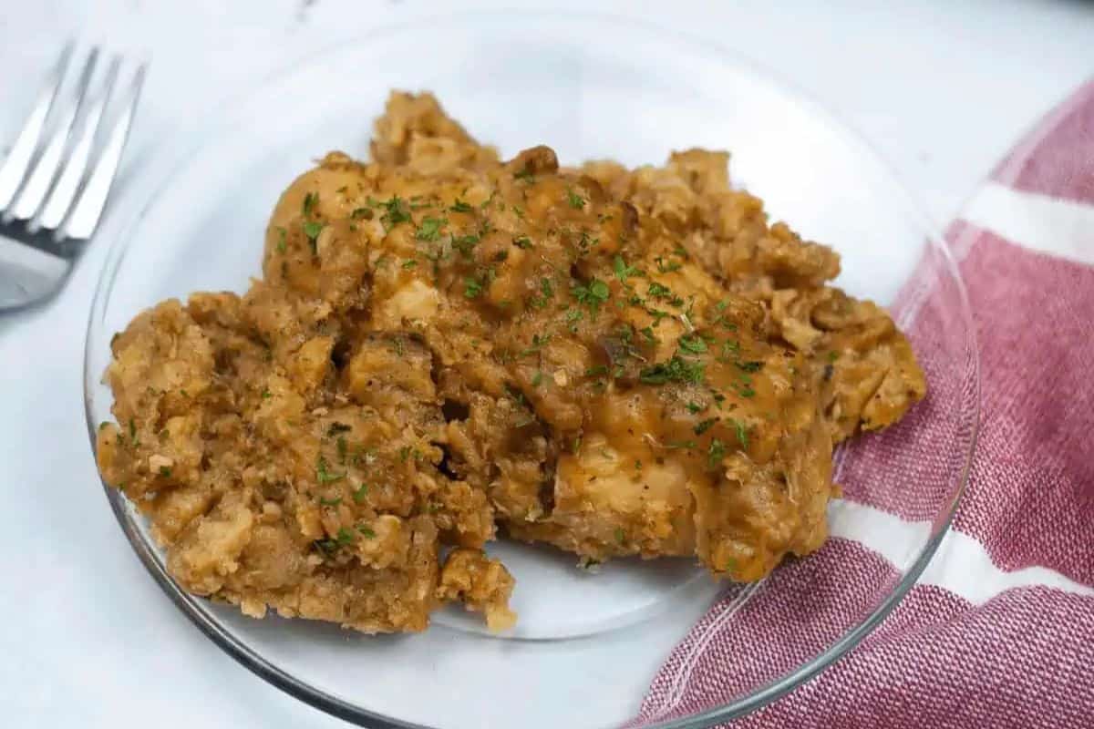 A serving of baked chicken and stuffing casserole on a glass plate, garnished with herbs, next to a red and white striped cloth—perfect comfort food for those who love comforting fall meals.