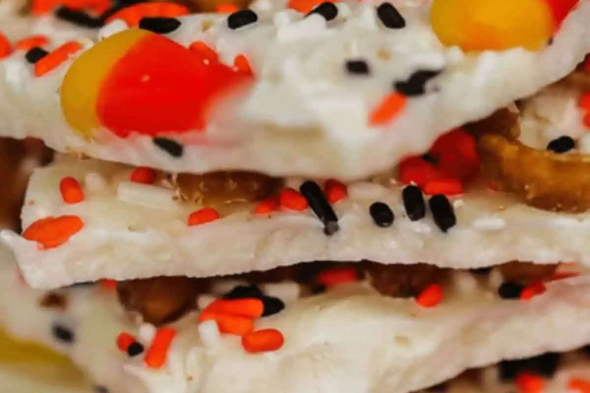 Close-up of stacked white chocolate bark pieces topped with Halloween-themed sprinkles, candy corn, and festive flair.