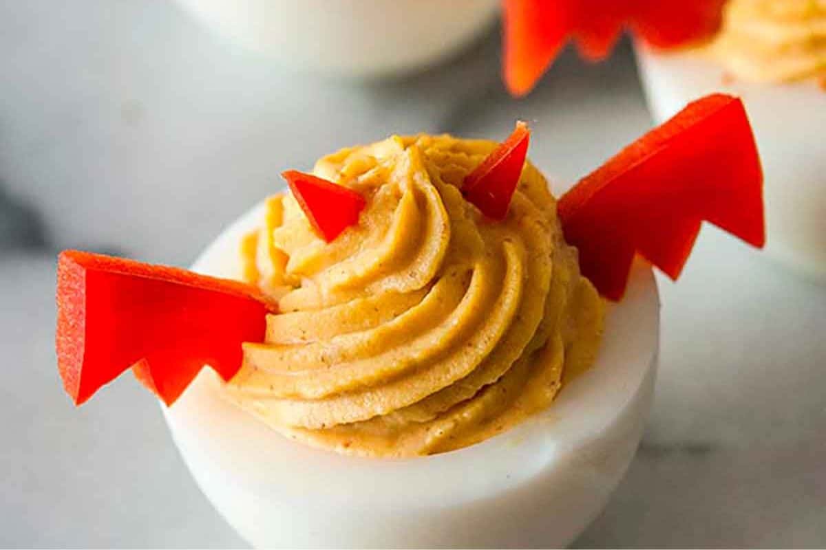 Deviled eggs styled for Halloween with spooky decorations, including dark bat-like wings.