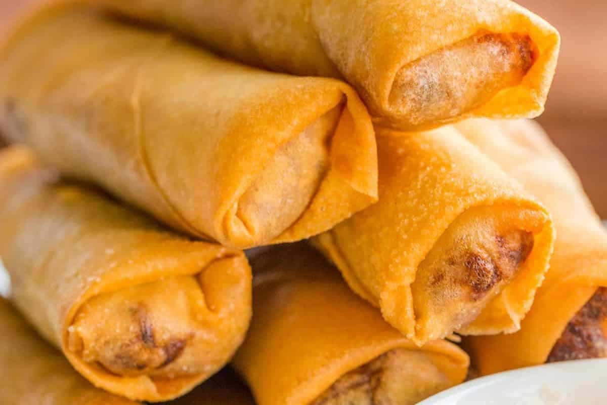 A close-up of a stack of golden-brown fried spring rolls, showing their crispy texture and tightly wrapped edges—a must try for fans of Asian dishes.