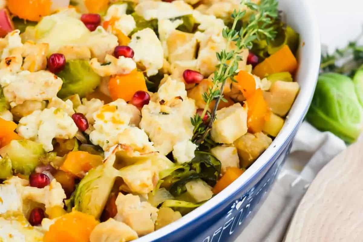 A casserole dish filled with chopped vegetables, chunks of cheese, pomegranate seeds, and garnished with a sprig of fresh thyme—perfect for comforting meals and cozy fall recipes.