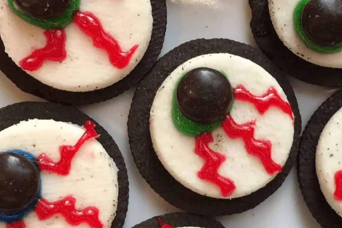 A close-up of several Halloween treats made from Oreo cookies. The top cookie has been replaced with white frosting, a red gel to look like veins, and a chocolate candy in the center to look like a monster eyeball.